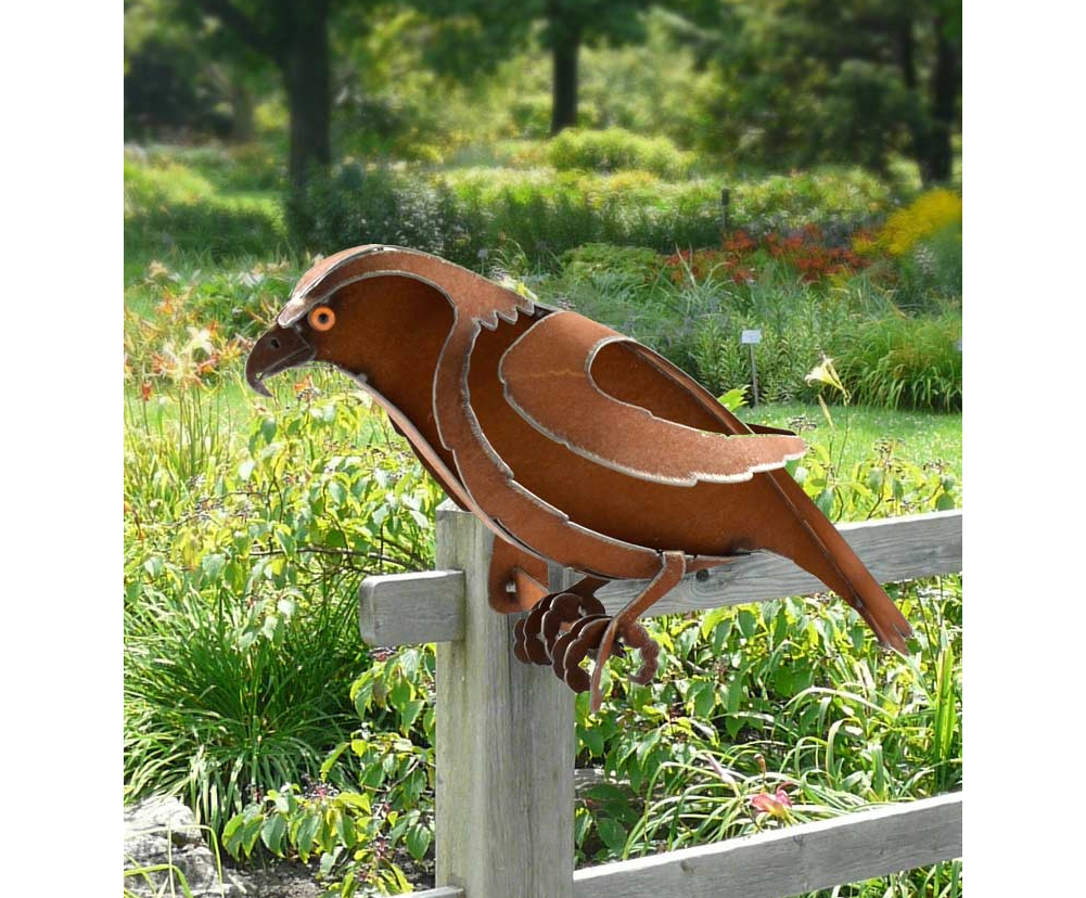 metal hawk sculpture against a wooden fence in a garden